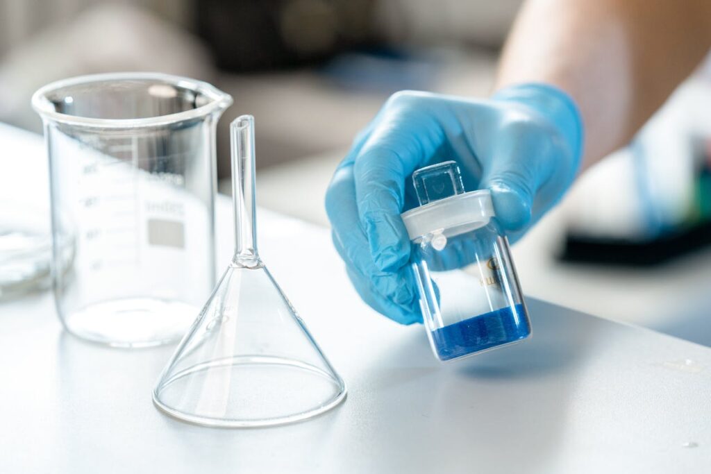 pexels-photo-9629678 Scientist holding vial with blue liquid next to beaker and funnel in lab.
